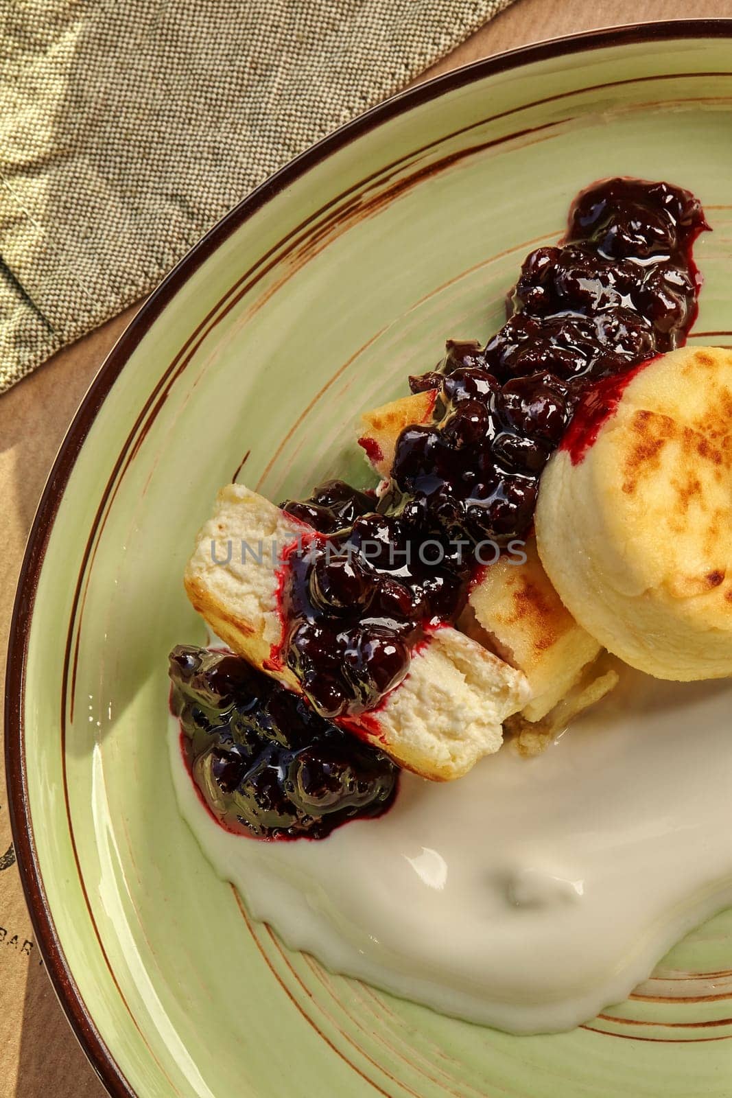 Homemade sweet syrniki topped with creamy cheese cream and rich berry jam, served on rustic ceramic plate
