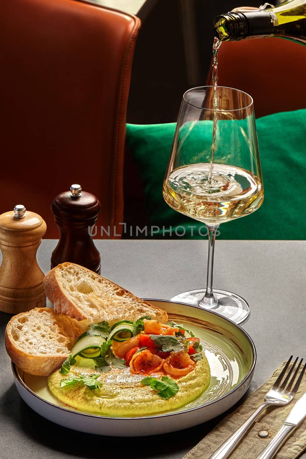 Elegant dinning setting with plate of creamy hummus complemented perfectly with white wine, served with succulent fried shrimps, fresh cucumber slices, greens and crispy toasts