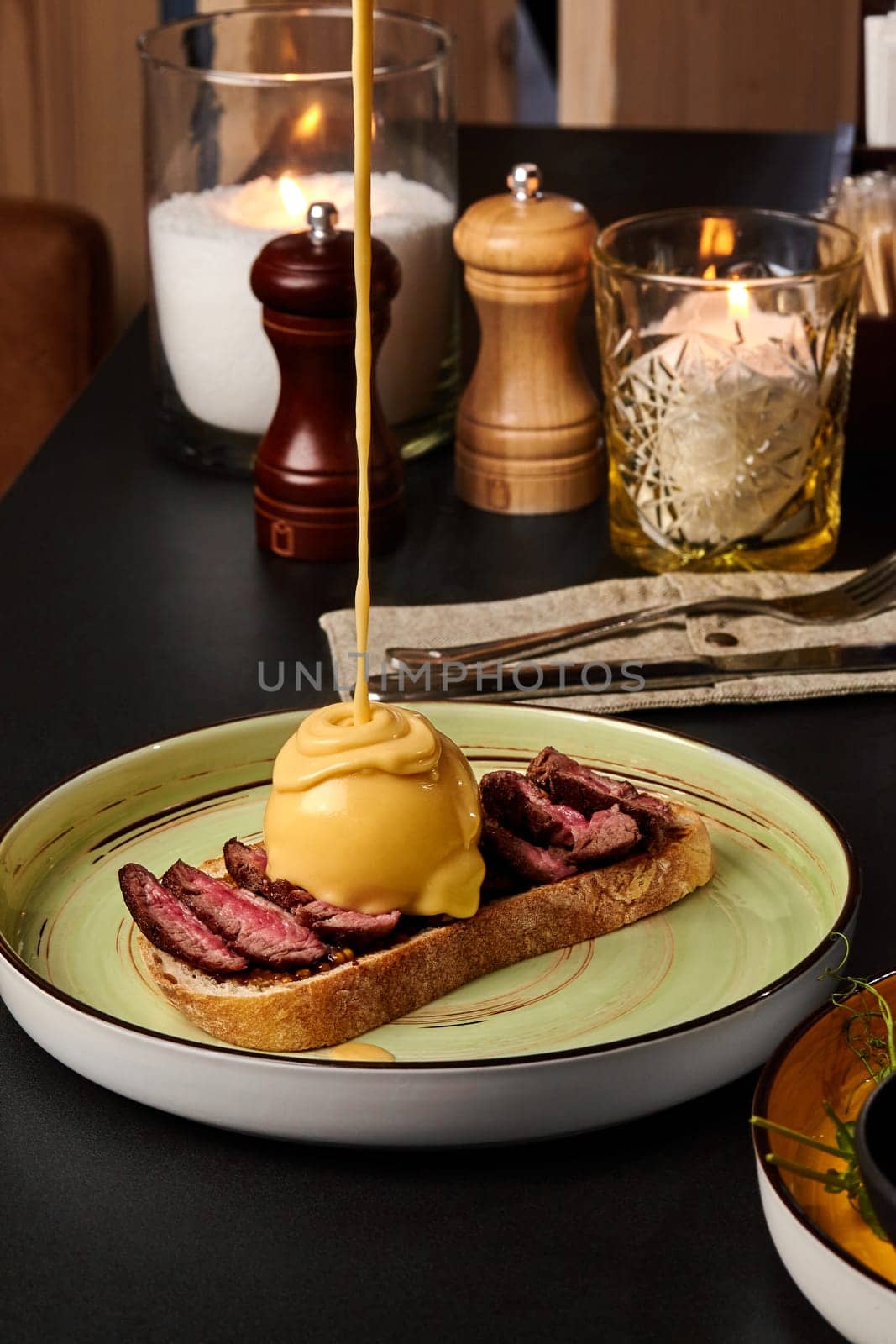 Perfectly cooked beef steak slices on toasted bread with poached egg topped with velvety hollandaise sauce, presented on ceramic plate in intimate dining setting