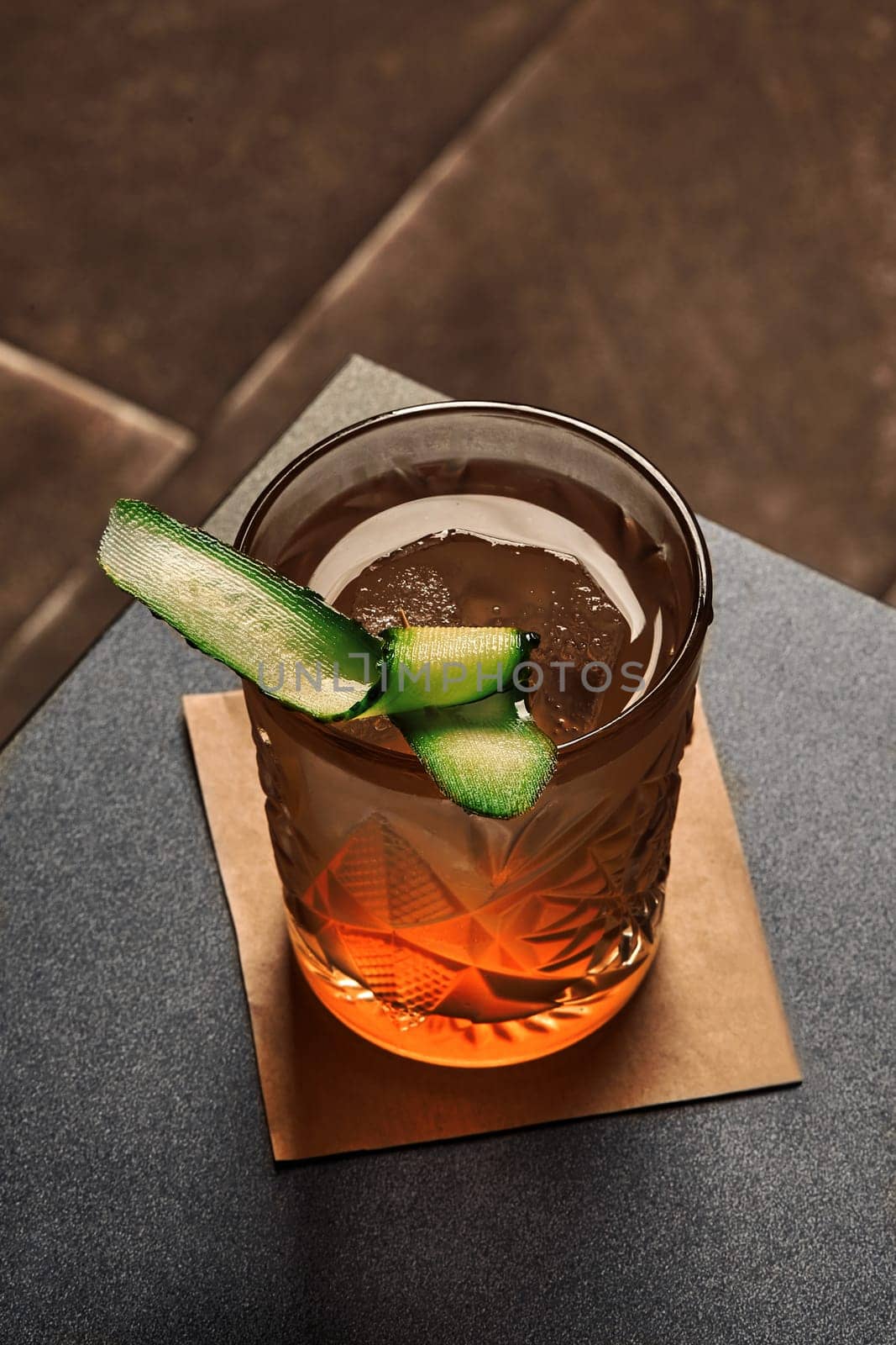 Glass of refreshingly herbal and floral gin garden cocktail garnished with fresh cucumber slice served on dark table, perfect for pre-dinner sipping