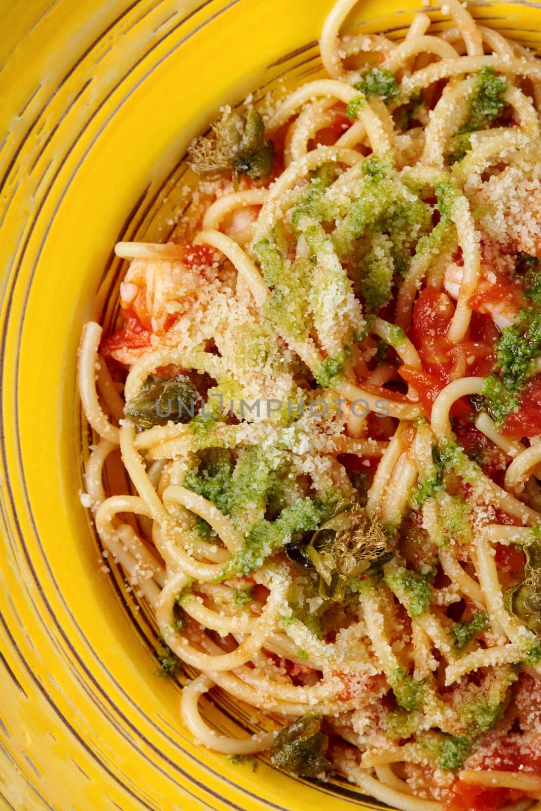 Closeup of colorful rich Italian style Arrabbiata Pasta with shrimp and crispy caper chips, seasoned with fragrant spicy tomato, chili and garlic sauce, sprinkled with grated parmesan, on yellow plate