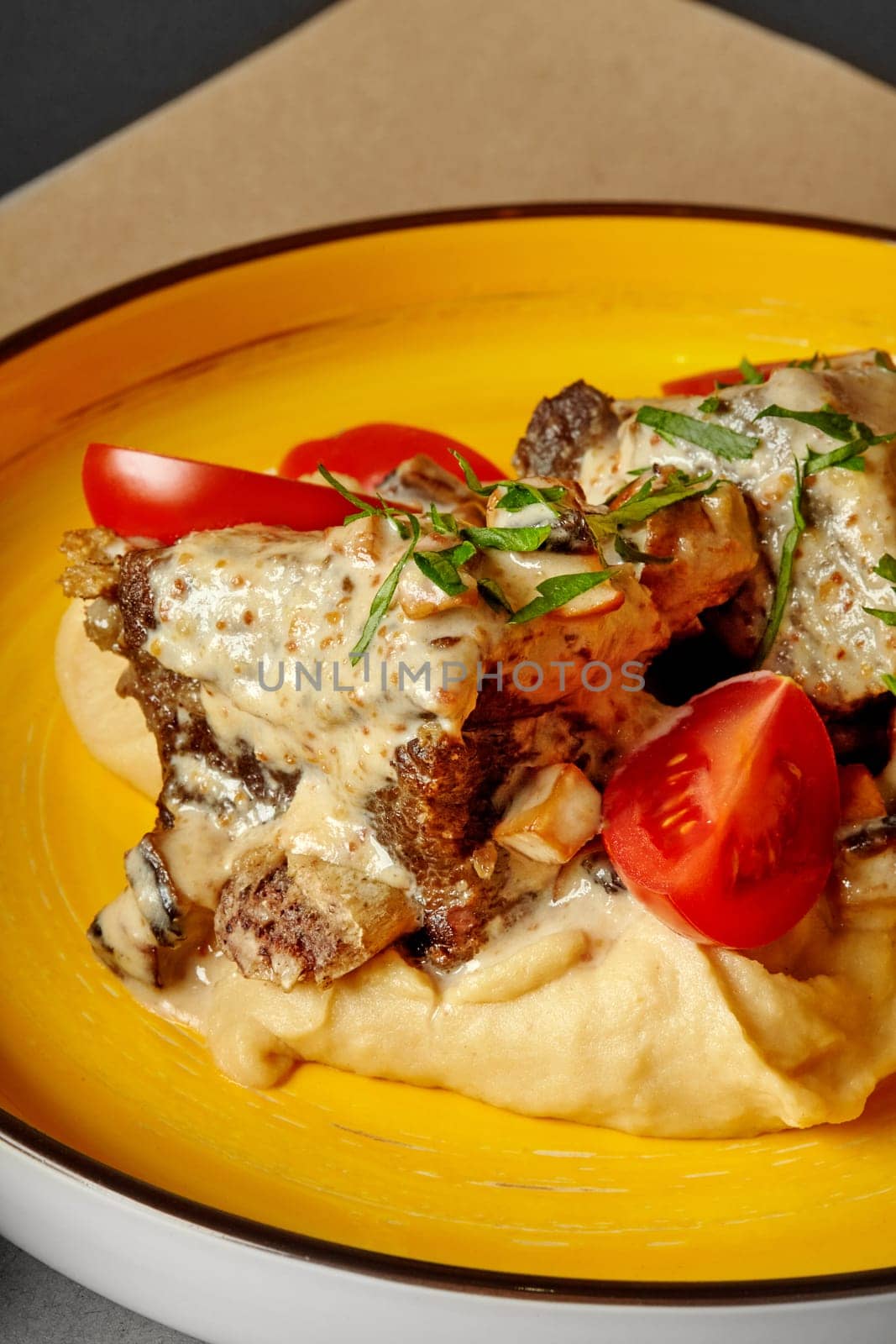 Spicy braised veal ribs dressed with creamy mushroom sauce served on bed of peanut puree with cherry tomatoes and greens on vibrant yellow ceramic plate