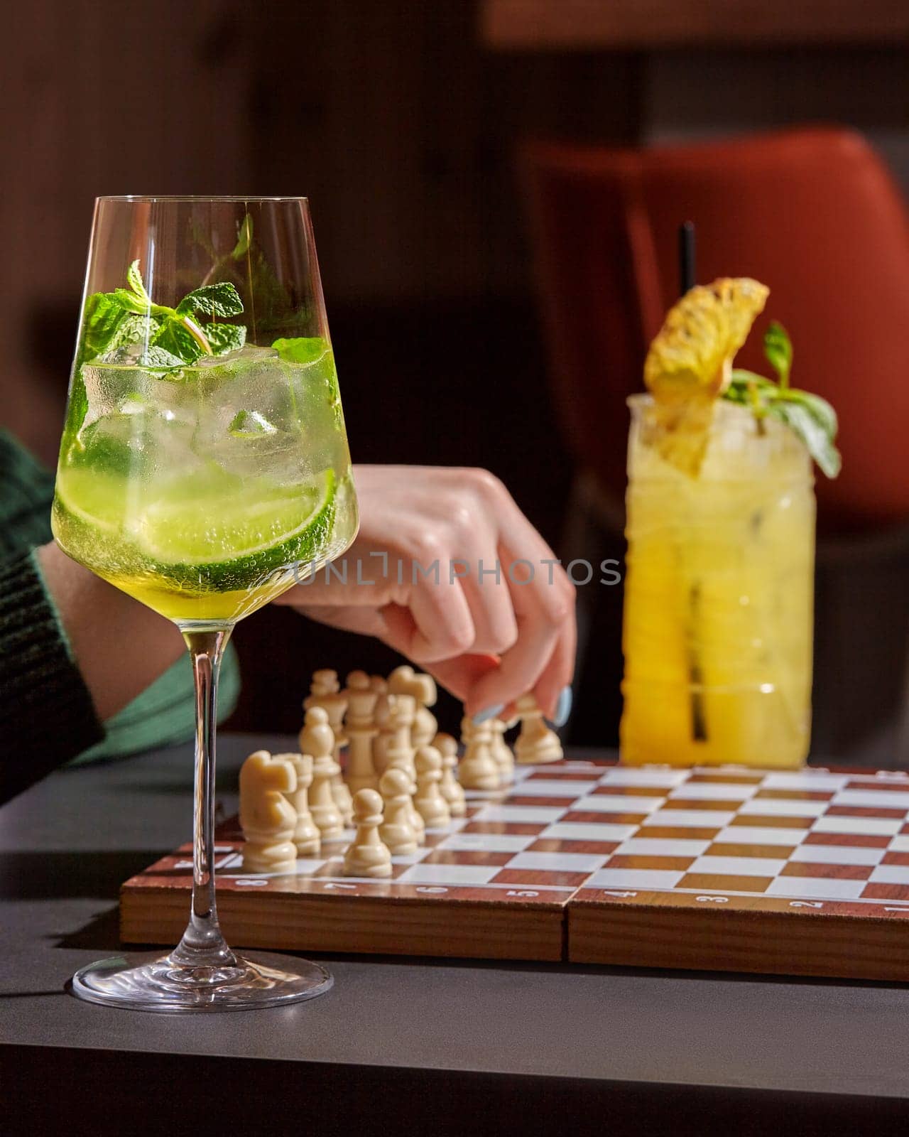 Classic refreshing Hugo cocktail with sparkling wine, fresh mint, lime and ice cubes in stem glass to accompany leisurely chess game in cozy relaxed atmosphere