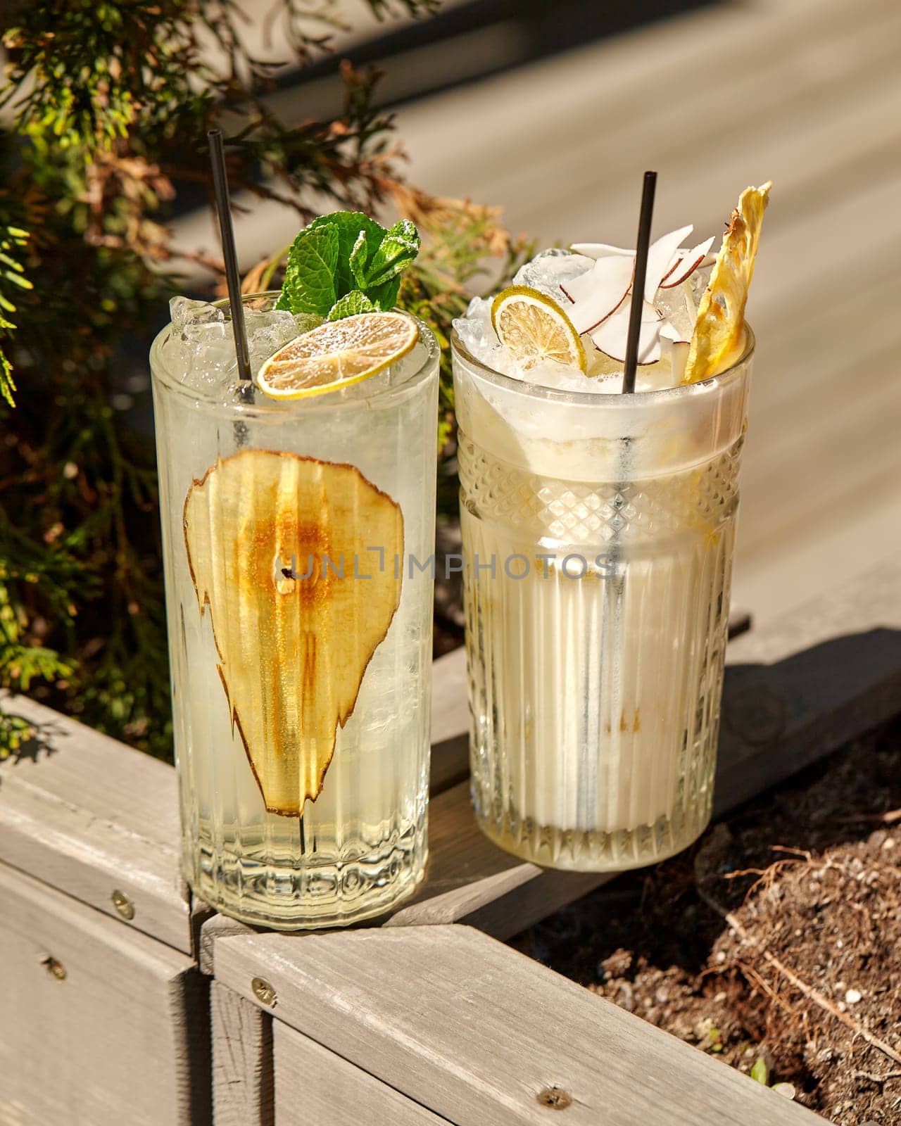 Sunlit glasses of pear lemonade and sweet creamy non-alcoholic pina colada cocktail with tropical flavours of pineapple and coconut garnished with fruits served outdoors for refreshing break