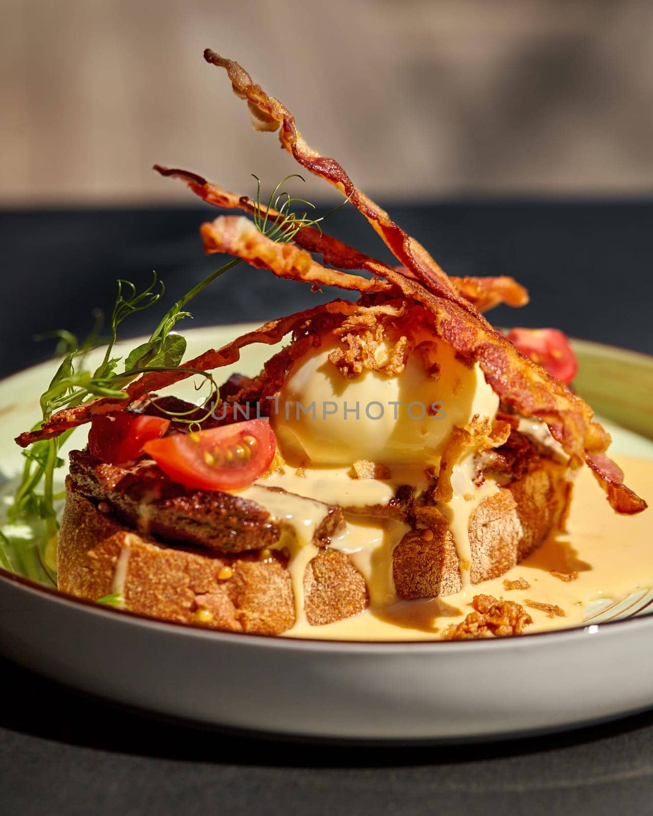 Close-up of savory Mediterranean-style bruschetta with slices of veal steak, crispy bacon strips, poached egg, spicy piquant sauce and fried onions, garnished with fresh cherry tomatoes and greens