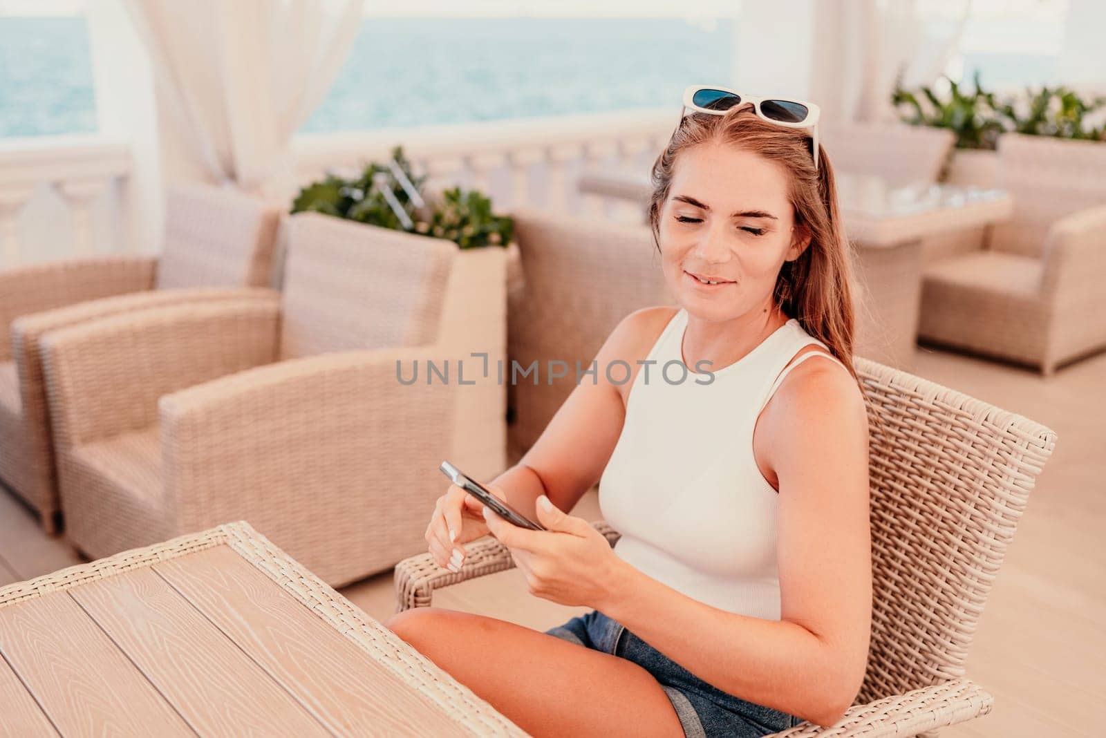 A woman is sitting at a table with a cell phone in her hand. She is taking a picture of the ocean