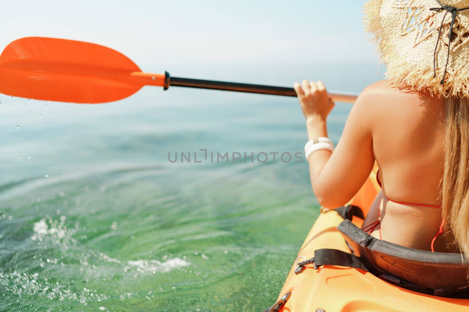 Woman in kayak back view. Happy woman with long hair in a swimsuit and hat floating in kayak on the sea. Summer holiday vacation. Summer holidays vacation at sea