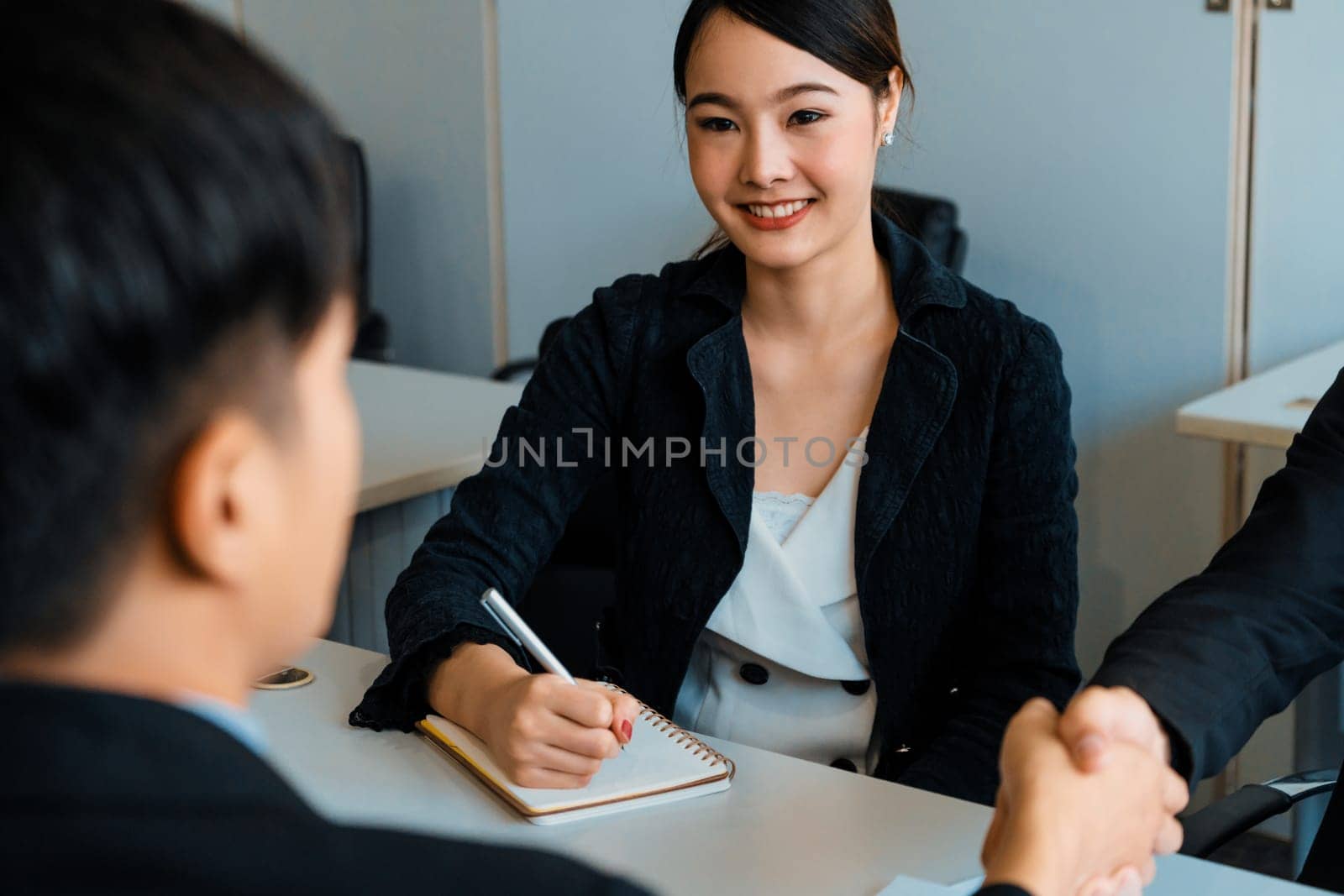 Business people agreement concept. Asian Businessman do handshake with another businessman in the office meeting room. Young Asian secretary lady sits beside him. uds