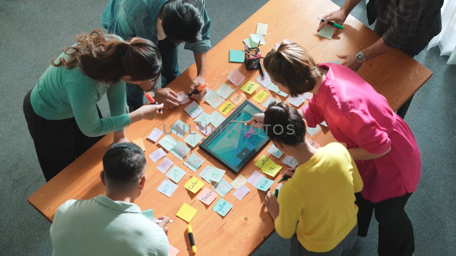 Top view of manager writing idea on sticky notes and explain idea about web design. Professional marketing team or programmer brainstorming idea while looking at tablet with color palette. Symposium.