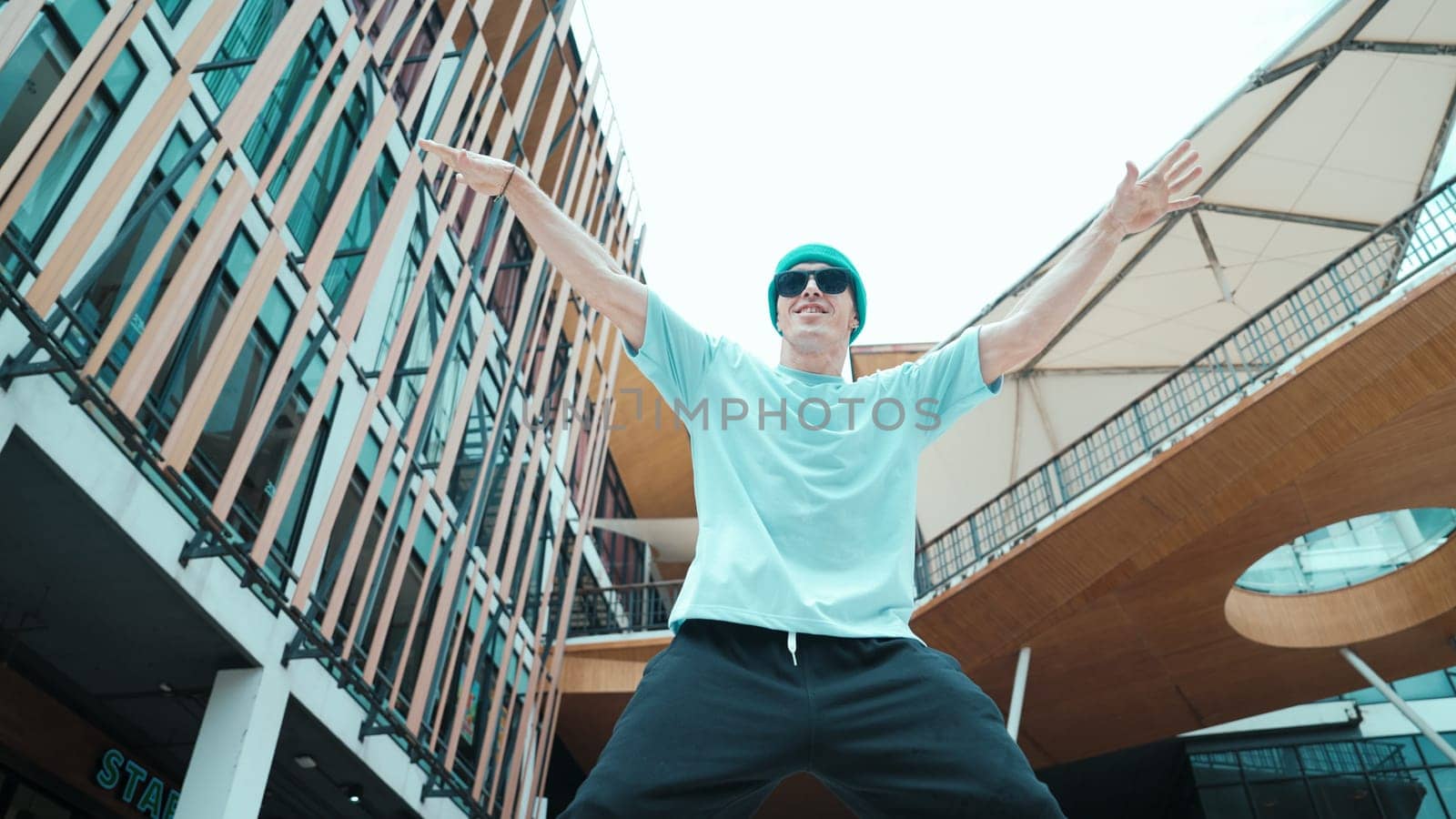 Portrait of caucasian street dancer looking at camera. Young attractive man moving, dancing practicing hip hop performance at modern mall. Low angle. Freestyle dance. Outdoor sport 2024. Endeavor.
