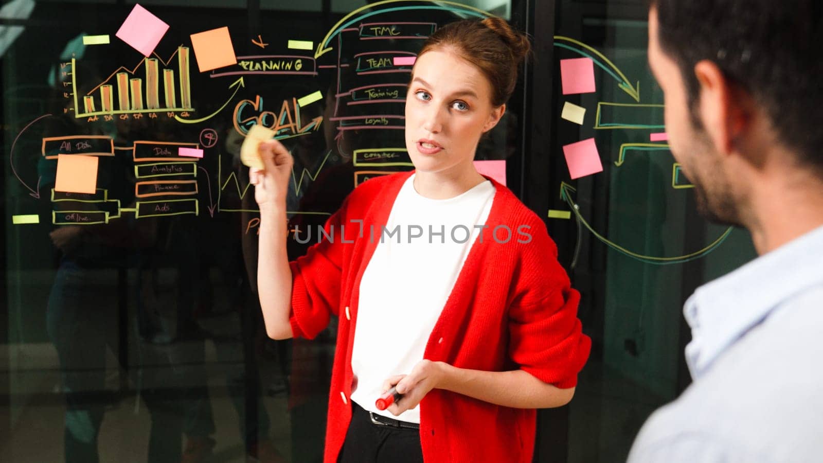 Closeup of young beautiful project manager present graph and business plan on glass wall. Skilled businesswoman show marketing strategy. Leader sharing brainstorming ideas to investor. Tracery