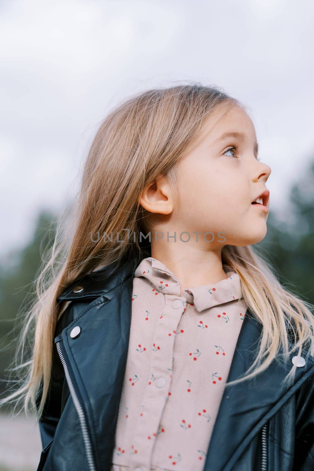 Little girl stands in the park with her head turned to the side. Portrait. High quality photo