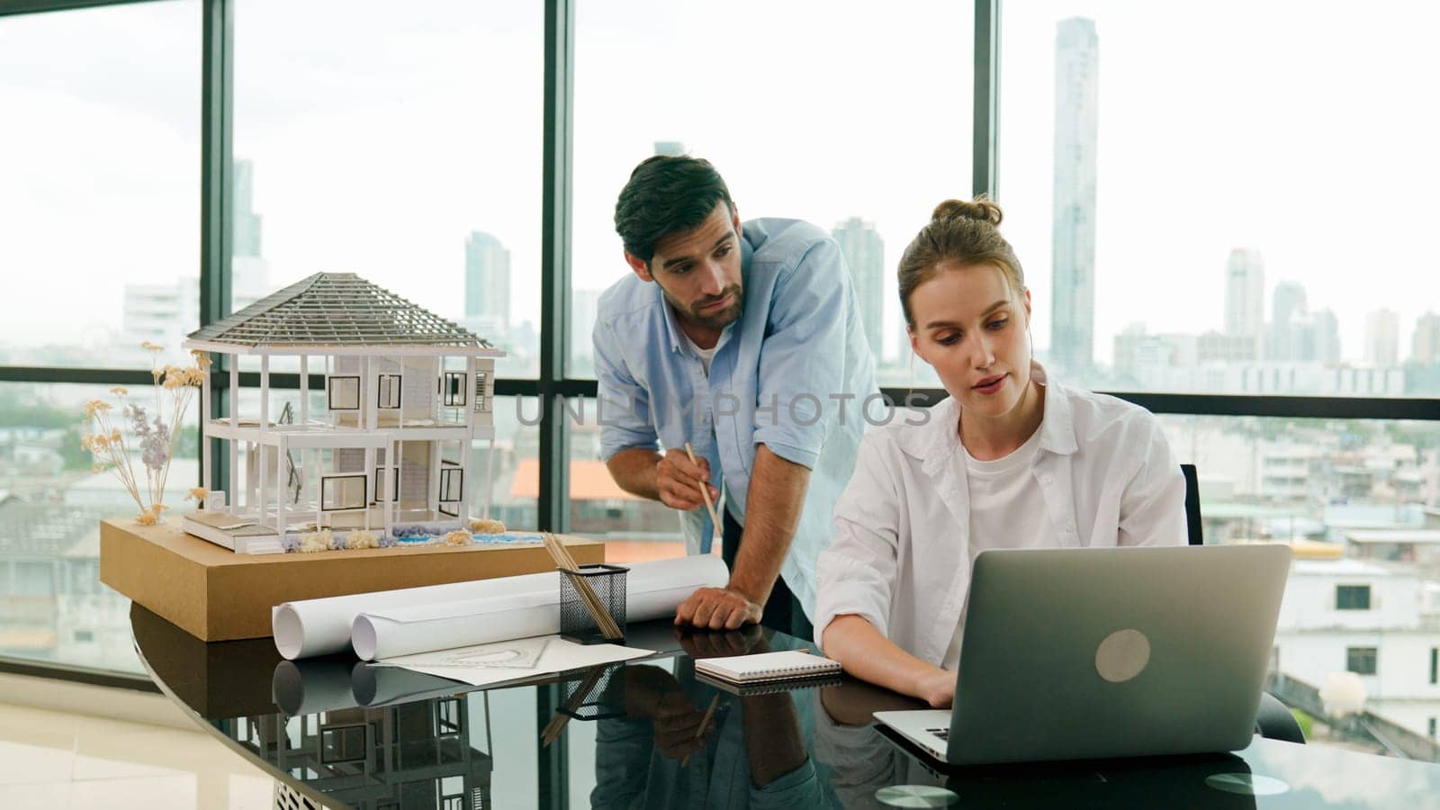 Smart architect engineer inspect house model while colleague using laptop analysis data. Professional designer team working together to design house model construction at modern office. Tracery