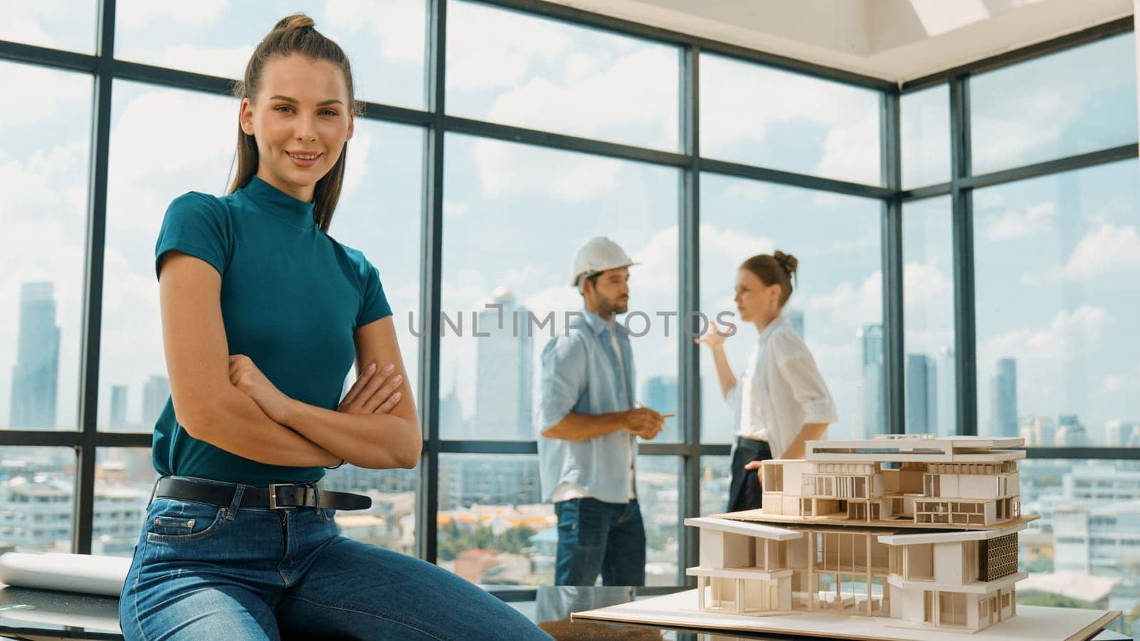 Young beautiful interior designer crossing arms while engineer team talking about house design. Skilled businesswoman smiling at camera with confident while sitting near house model. Tracery