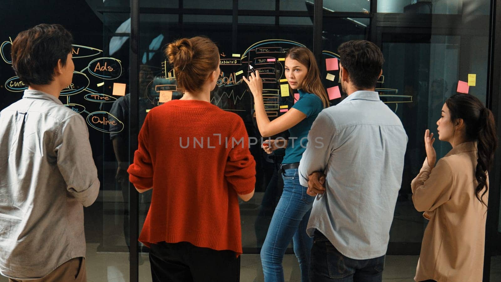 Executive manager pointing at business idea to present diverse investor team. Businesspeople listening female leader present marketing strategy while using sticky notes and mind mapping. Tracery