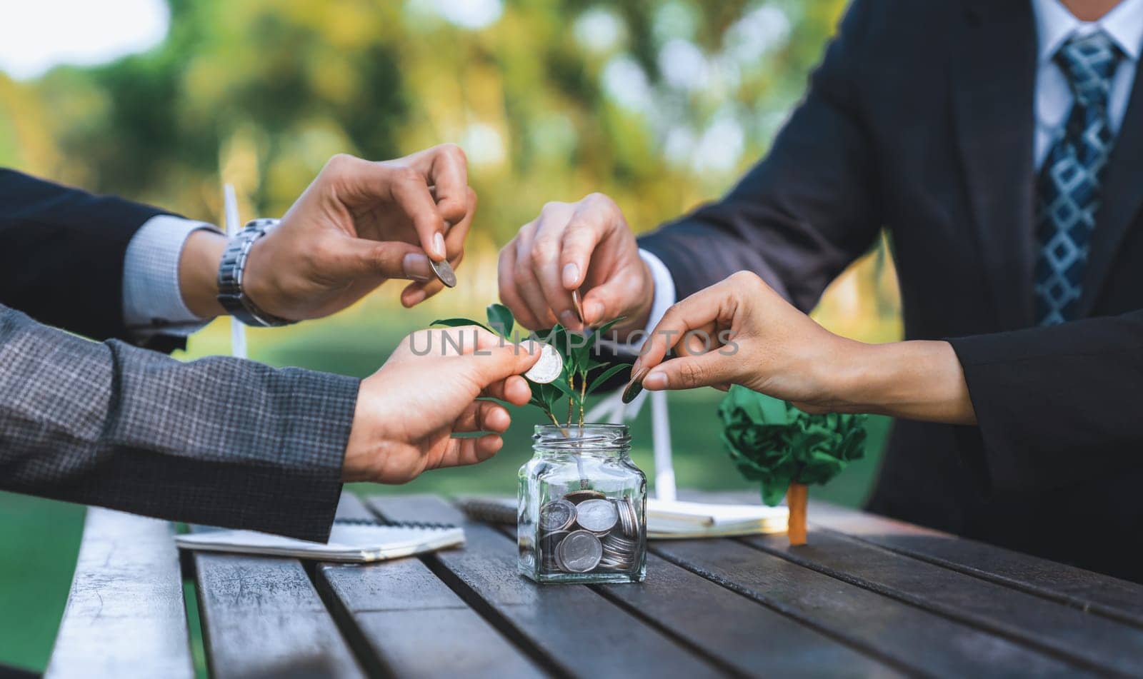 Business people put coin to money saving glass jar on outdoor table as sustainable money growth investment or eco-subsidize. Green corporate promot and invest in environmental awareness. Gyre
