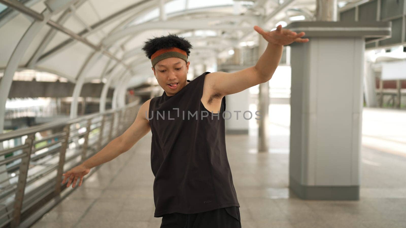 Smart handsome dancer moving hands while dance to hip hop music. Professional asian hipster wearing headphone while walking along the corridor with blurring background. Outdoor sport 2024. Sprightly.