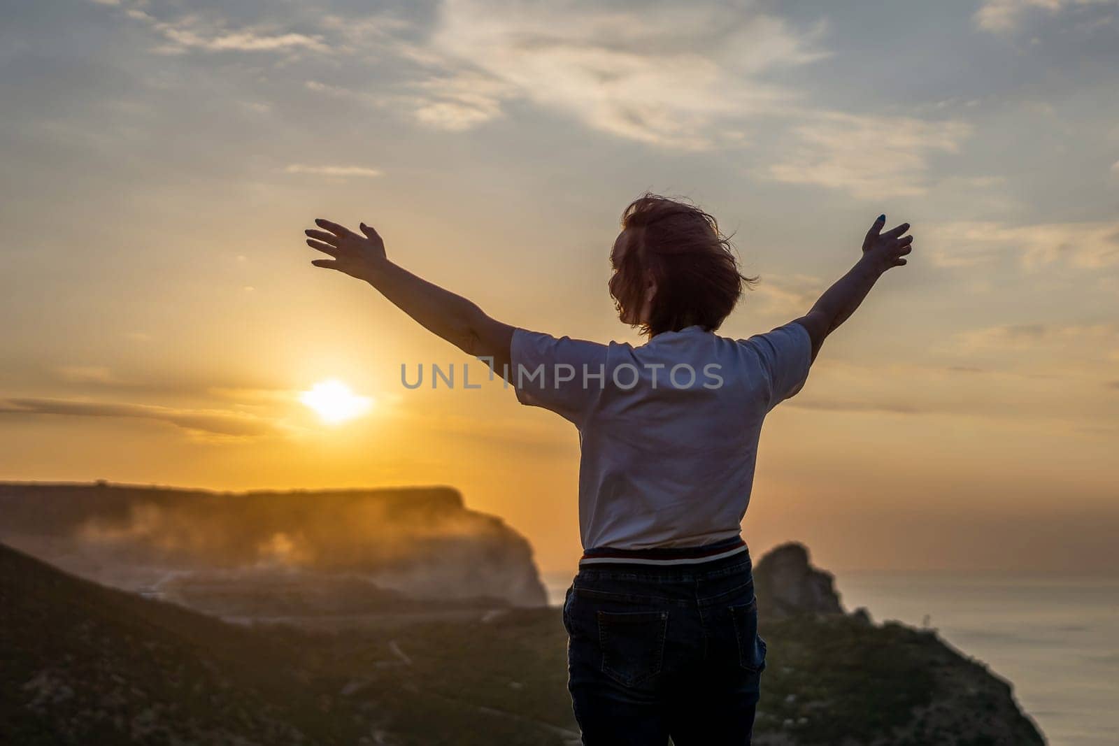 Happy woman on sunset in mountains. Woman standing with her back on the sunset in nature in summer with open hands. Silhouette