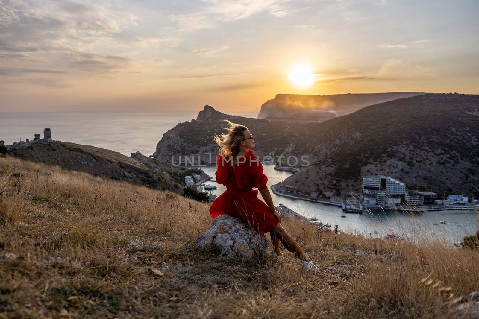 Woman sunset sea mountains. Happy woman siting with her back on the sunset in nature summer posing with mountains on sunset, silhouette. Woman in the mountains red dress, eco friendly, summer landscape active rest.