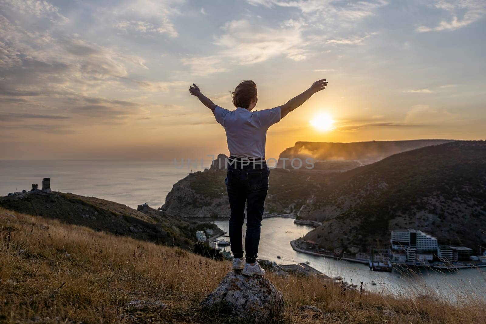 Happy woman on sunset in mountains. Woman standing with her back on the sunset in nature in summer with open hands. Silhouette. by Matiunina