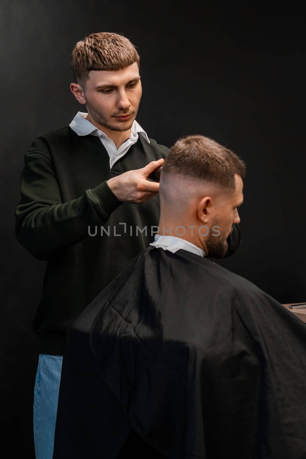 Skilled barber cuts client short hair with electrical trimmer in barbershop closeup. Hairdresser does stylish men haircut in beauty shop