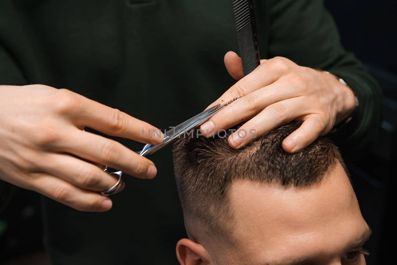 Hairstylist adeptly styles the clients brunette hair at the barbershop. by vladimka