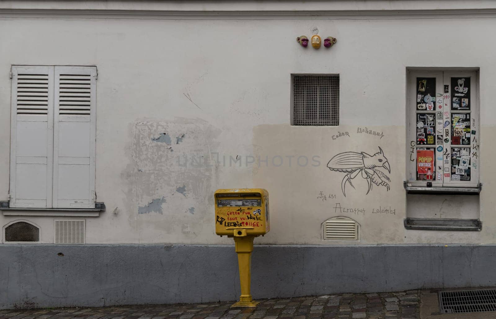 France, Paris - Jan 03, 2024 - Shutters and windows with small peephole on old wall of a ground floor residence and Post box. A narrow cobblestone street with typical French architecture descends and rises, Space for text, Selective focus.