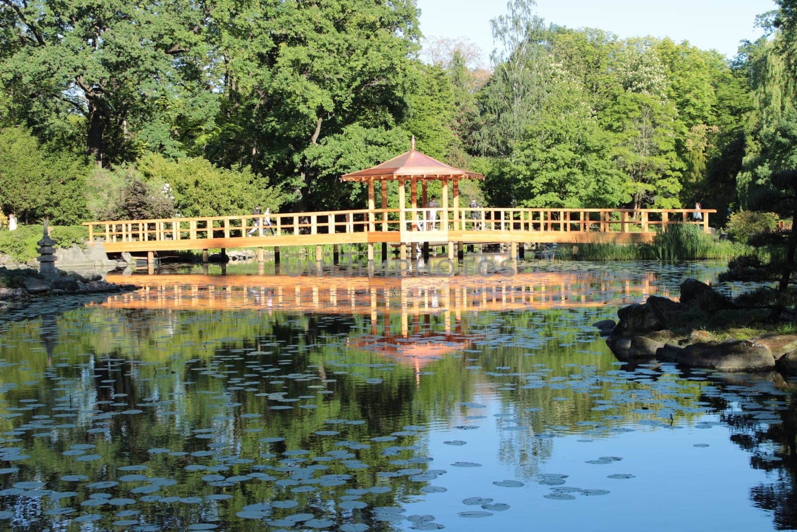 A wooden bridge and a gazebo across the river in a picturesque garden. High quality photo