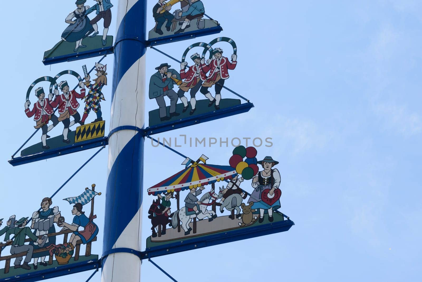 Traditional Bavarian maypole with colorful figures depicting local customs and festivities against a clear blue sky.