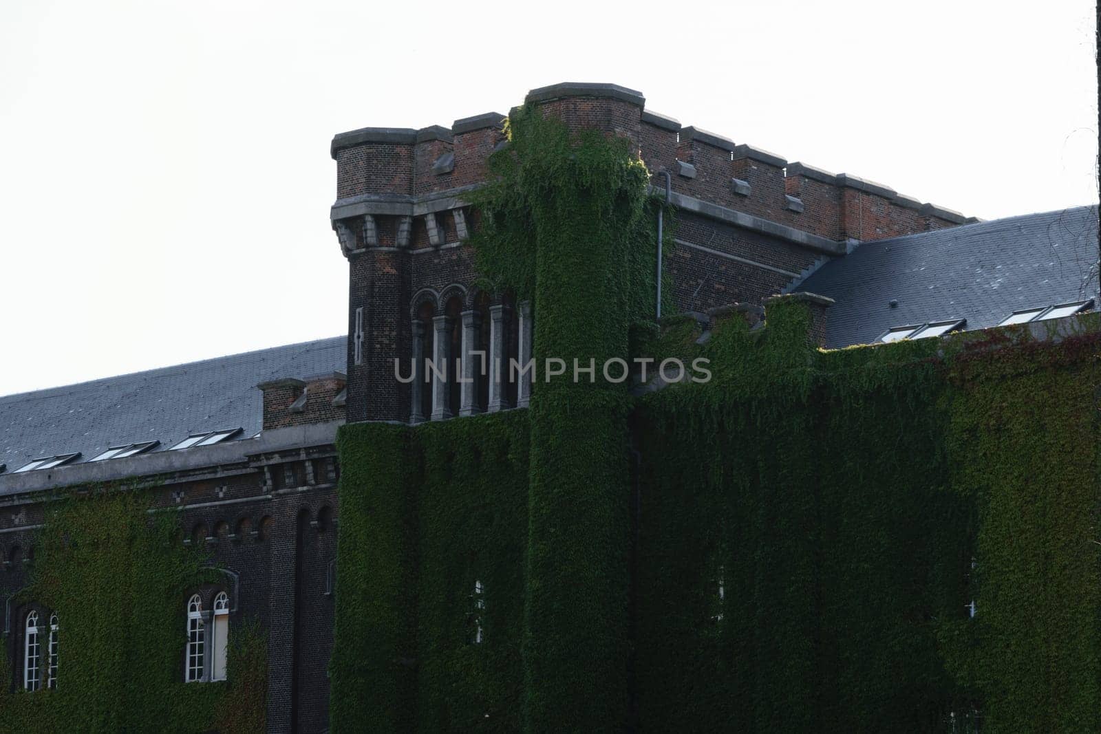 A historic brick building with ivy-covered walls and a tower, featuring windows and a slate roof.