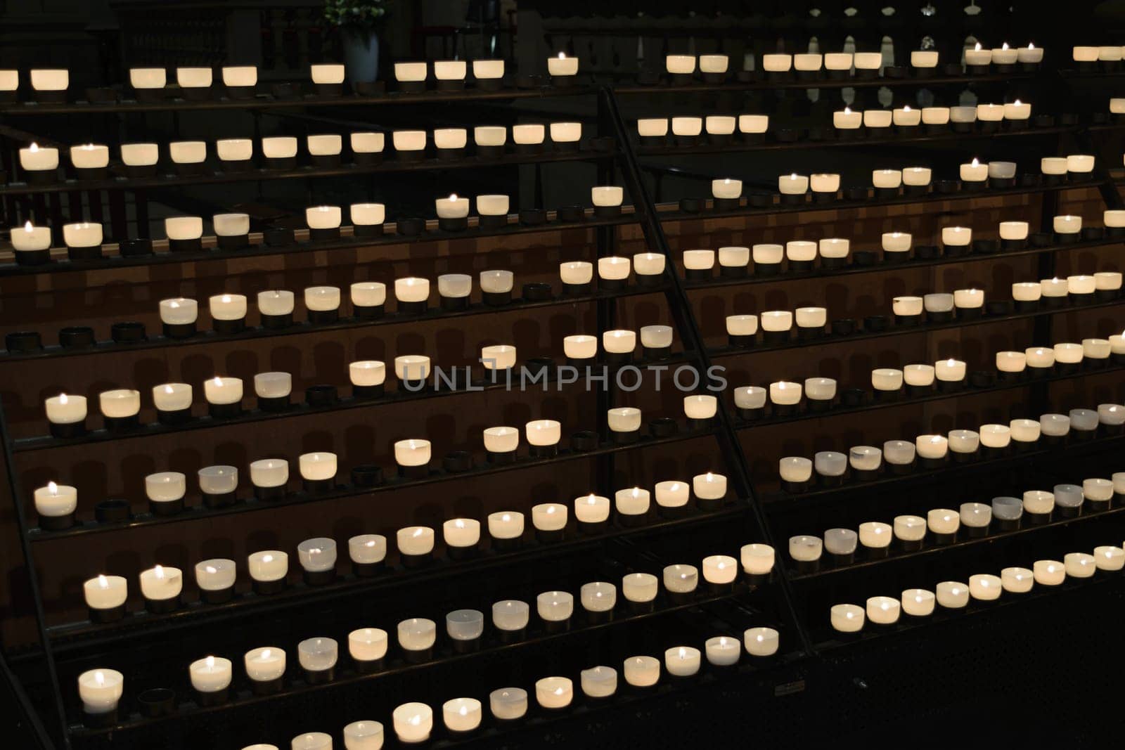 Rows of lit candles on a metal stand in a dimly lit setting.