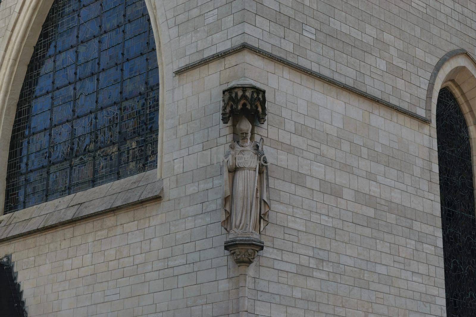 A stone statue of a religious figure on the exterior wall of a historic building with arched windows.