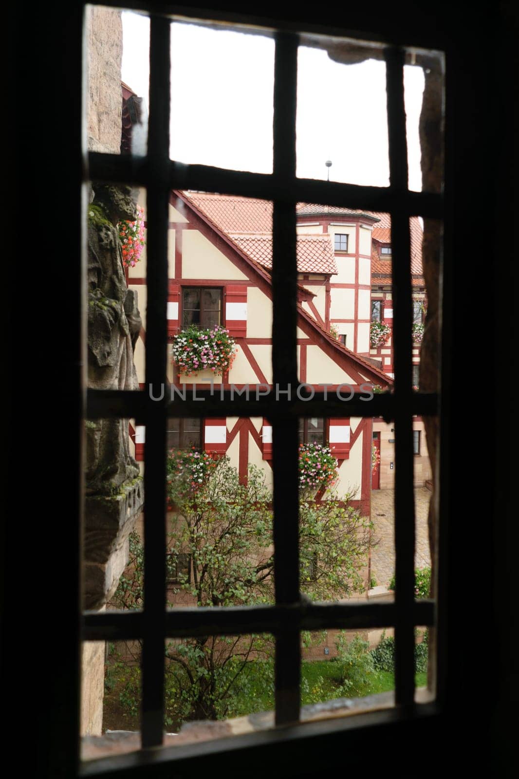 View through a window with bars, showing a traditional half-timbered house with flower boxes on the windows.