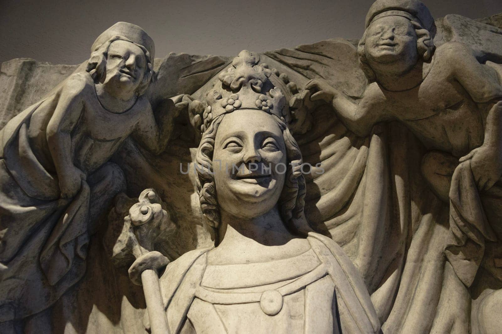 Close-up of a medieval stone sculpture depicting a crowned figure with a scepter, flanked by two smaller figures.