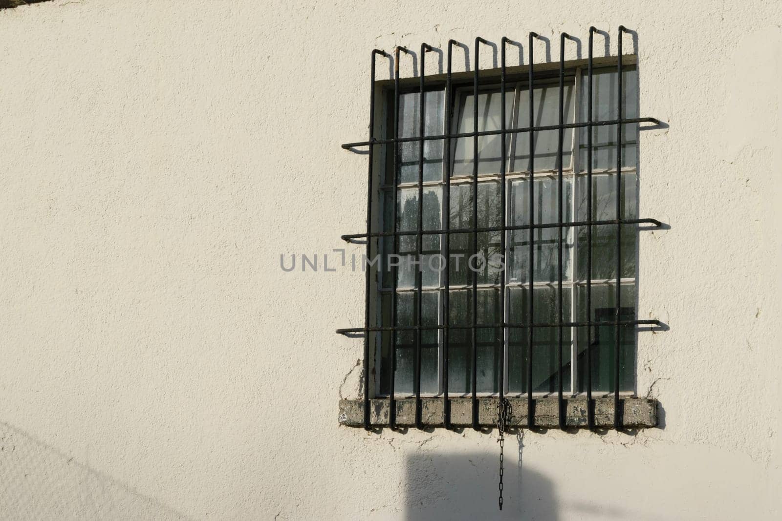 A small window with metal bars on a white concrete wall.