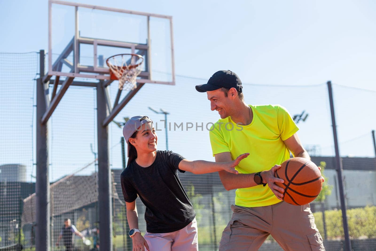 A happy father and teen daughter playing basketball outside at court. by Andelov13
