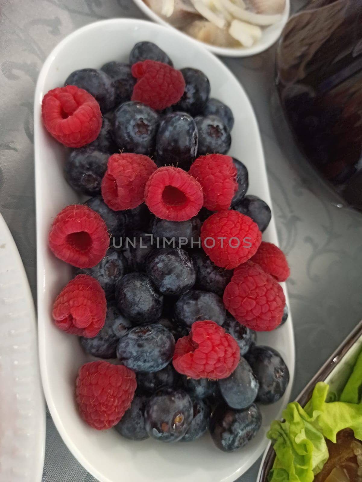 Spotted ceramic bowl with assortment berries blueberries, strawberries and blackberries at old black board over wooden table. Rustic style. Top view. Square image. High quality photo