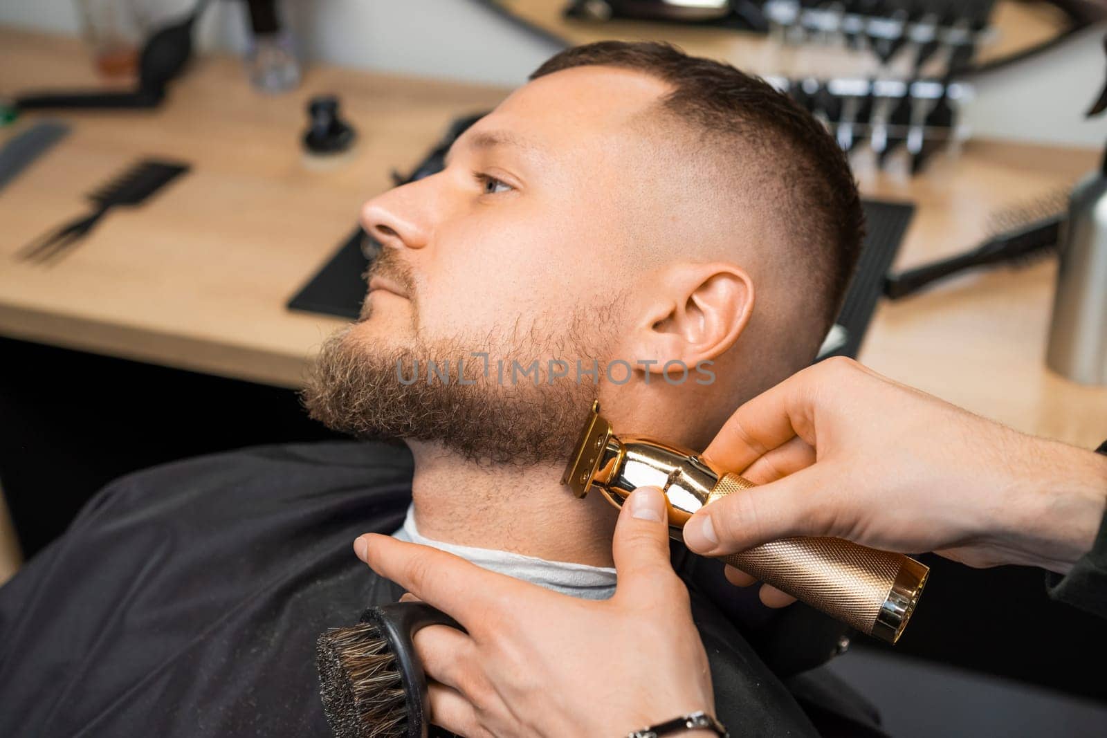 Barber skillfully uses a trimmer to shape the clients beard, focusing on the contours of the cheek.