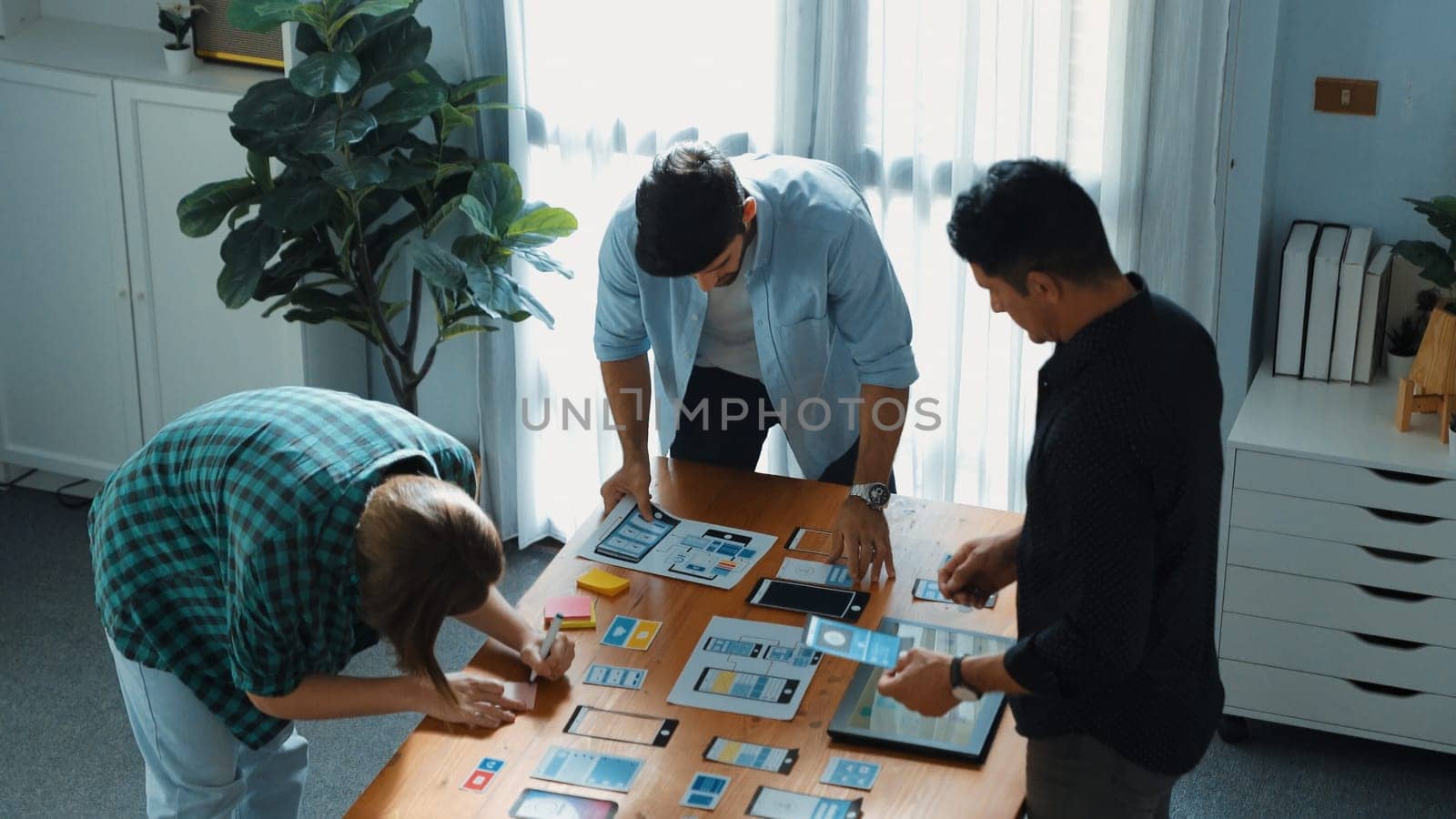 Top view of smart Ui designer brainstorming and planning about Ux Uo design or mobile interface wireframe design with diverse develop team. Caucasian programer walking and joining meeting.Convocation.