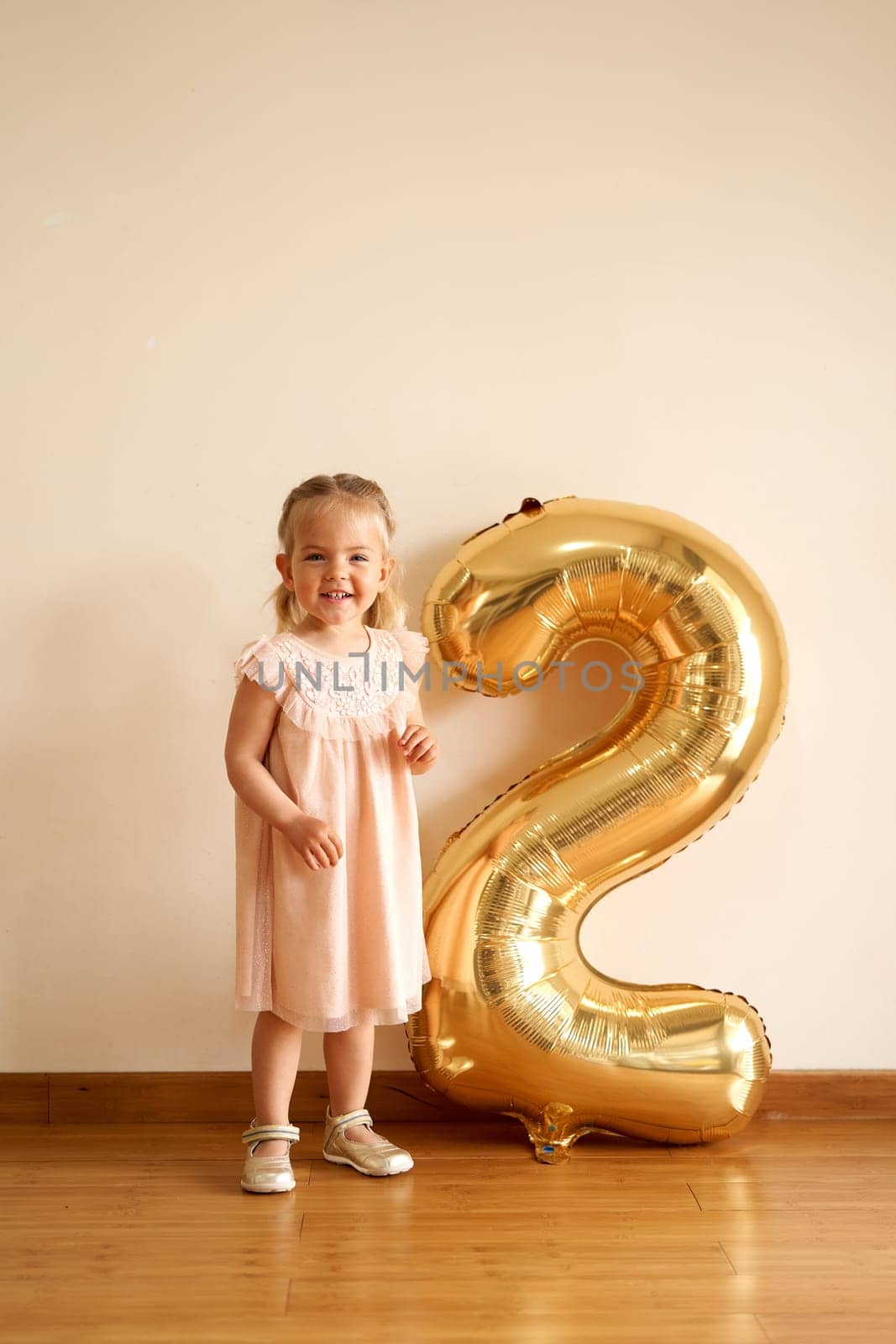 Little smiling girl stands near inflatable golden number two. High quality photo