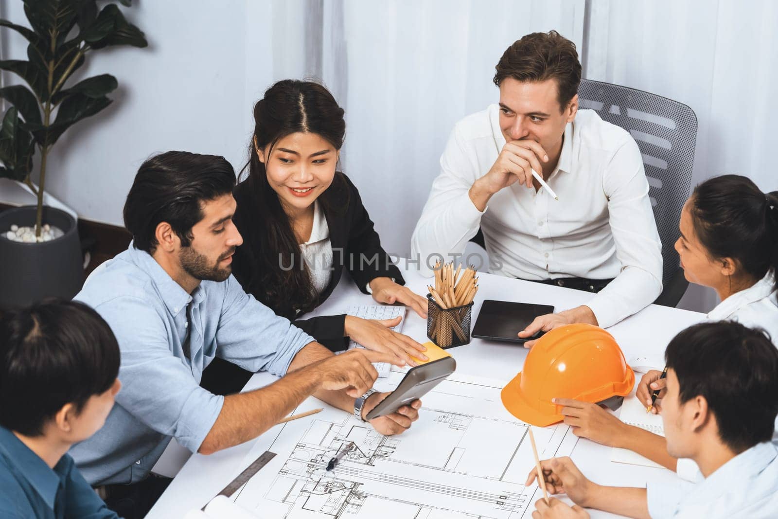 Diverse group of civil engineer and client working together on architectural project, reviewing construction plan and building blueprint at meeting table. Prudent