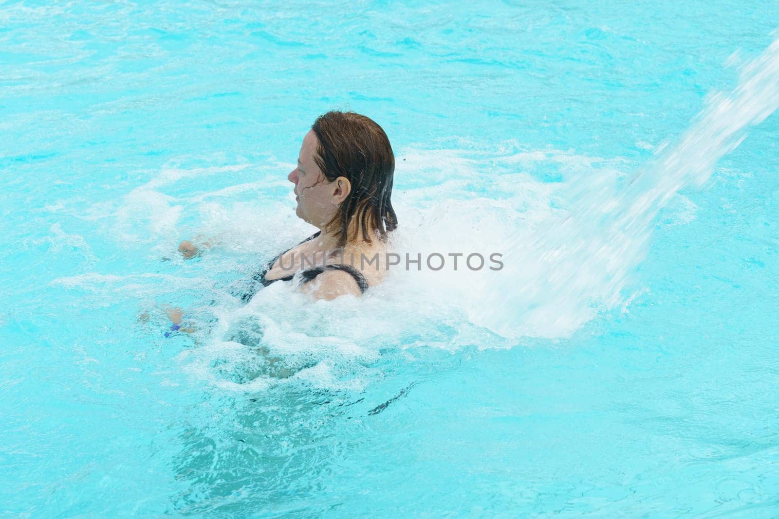 A woman is joyfully swimming in a pool as a refreshing spray of water cascades down, creating a fun and relaxing atmosphere.