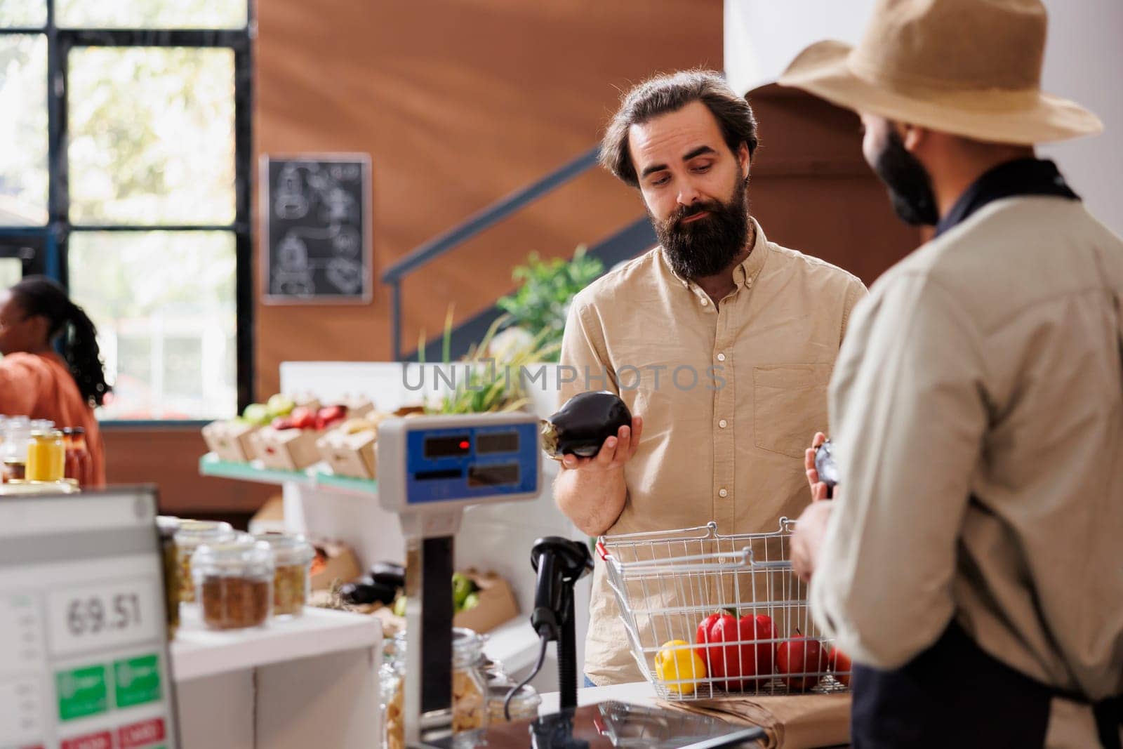 In local market, salesperson with an apron and hat assists a Caucasian shopper in purchasing fresh, eco-friendly produce. Healthy food options are plentiful, and the packaging is recyclable.