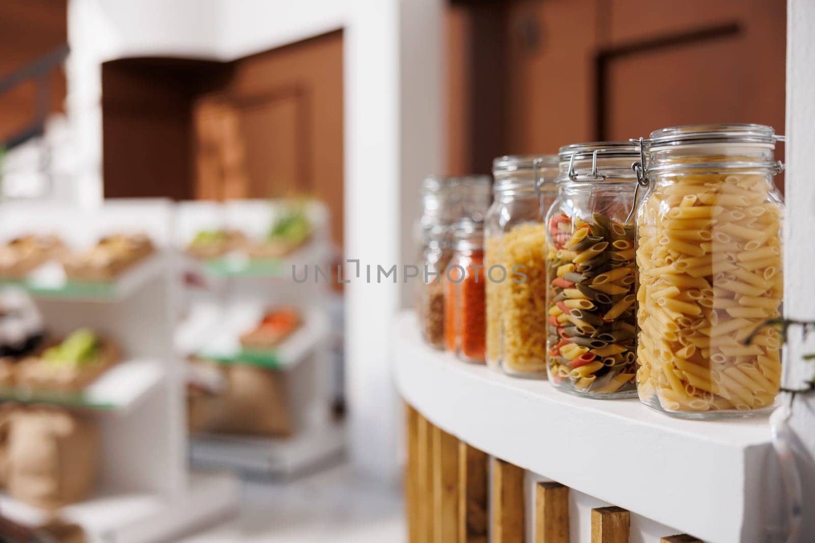 Close up shot of glass containers containing different kinds of pasta put on counter of eco friendly shop. In local supermarket, reusable plastic free jars show various organic bio food ingredients.