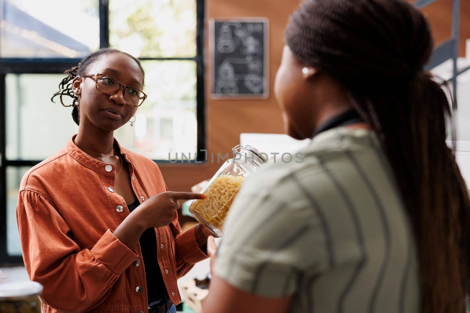 African American storekeeper chats with client wearing glasses at bio food market. Black women in local grocery store, discussing locally grown eco friendly produce for healthy lifestyle.
