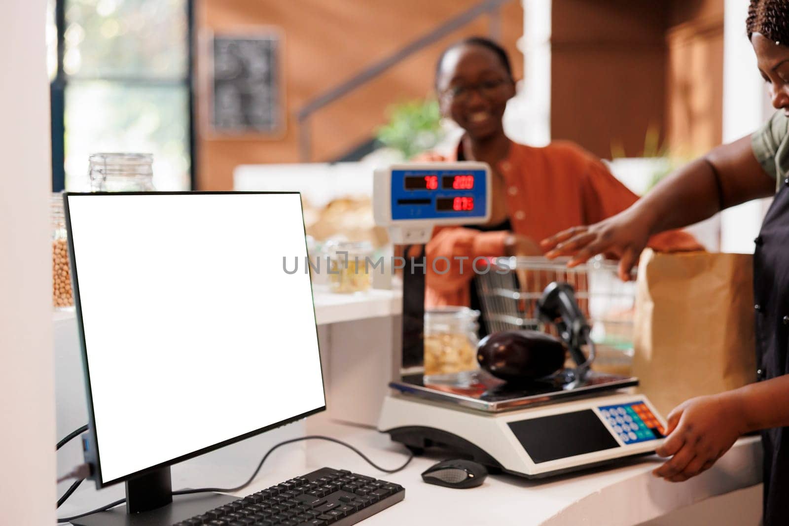 Seller using scale to measure organic products, with computer screen nearby having copy space display for bio food market commercial. Desktop computer at cashier desk showcasing blank mockup template.