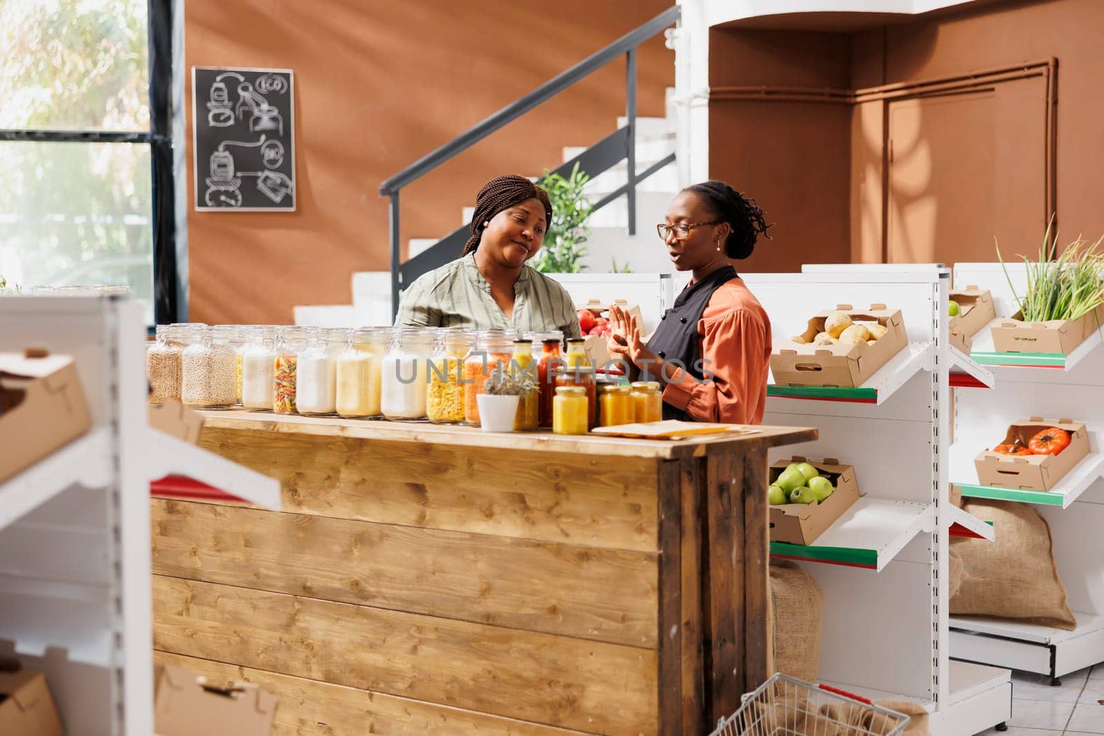 Female vendor with glasses showcasing her products in zero waste supermarket, selling eco friendly food to black consumer. Local trader selling her organic farm grown bulk products during event