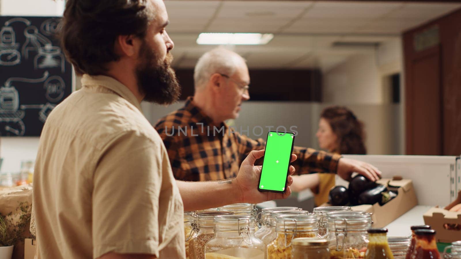 Man using green screen smartphone in zero waste supermarket to check ingredients for healthy recipe. Client in local grocery shop uses chroma key phone while shopping for organic veggies