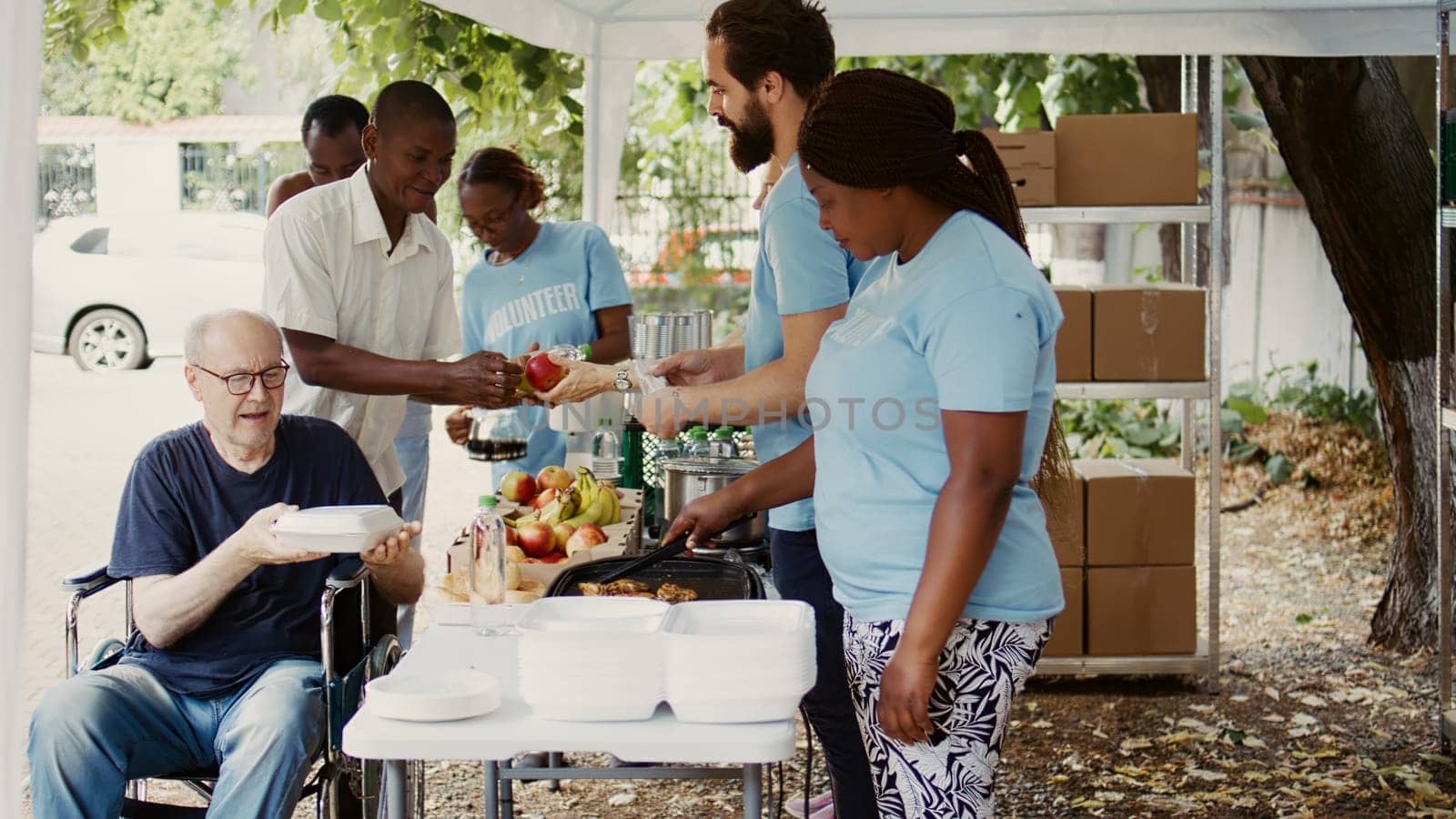 Group dedicated to charity helping out the poor giving away free food including fresh fruits to homeless people. Volunteers give assistance to alleviate hunger for disabled person in wheelchair.