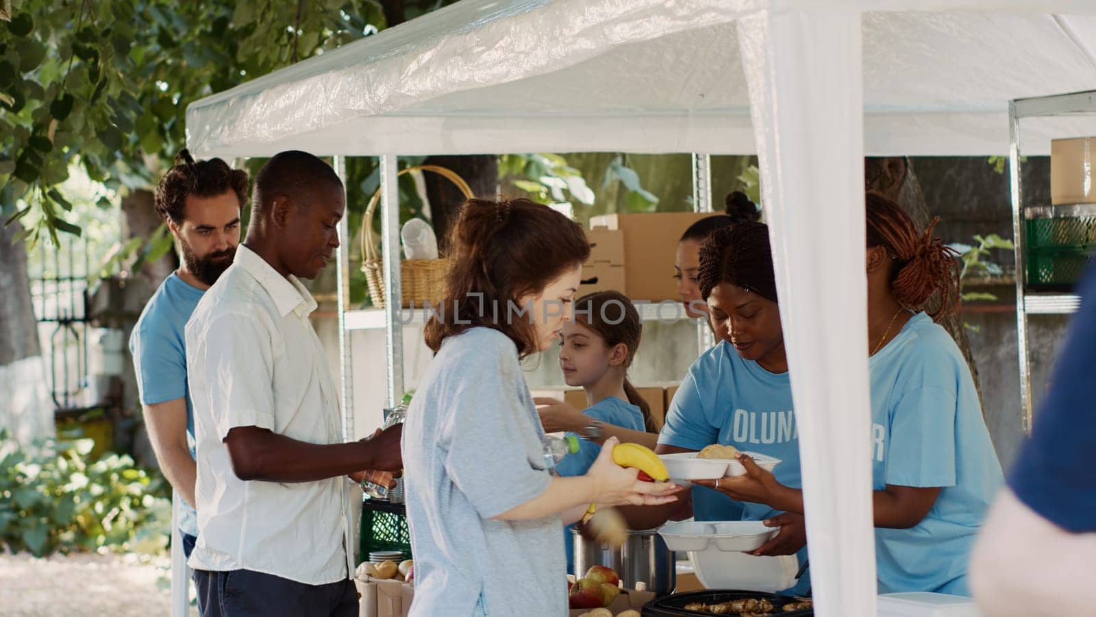 Friendly charity workers at food drive distributing necessities and free food to underprivileged. Voluntary individuals helping to fight hunger by providing hot meals to needy and homeless people.
